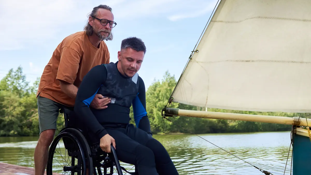 Mężczyzna podnoszący mężczyznę z wózka pomagający mu dostać się na łódź