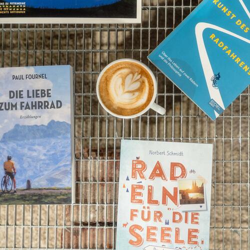 Bücher und Cappuccino auf Gitterrost, warme Erdtöne, blauer Himmel, Kaffeetassenmuster in Herzform, Fahrrad-Themen.