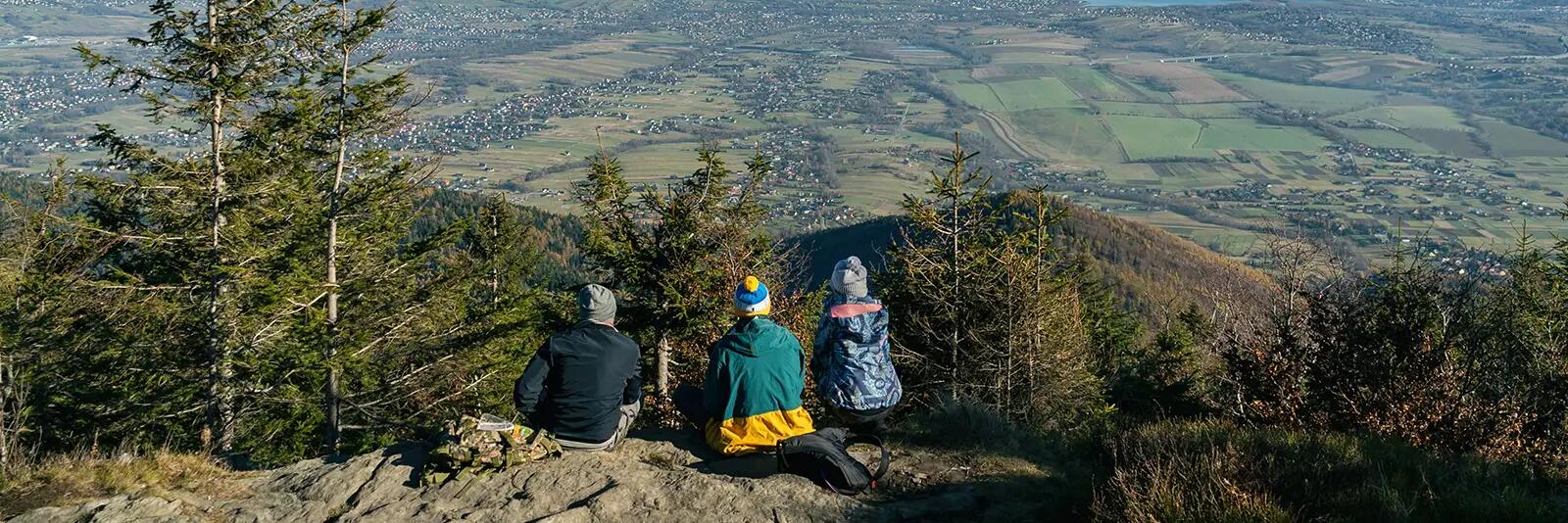 Ludzie siedzący na skale podziwiający widok na szczyty w Beskidach