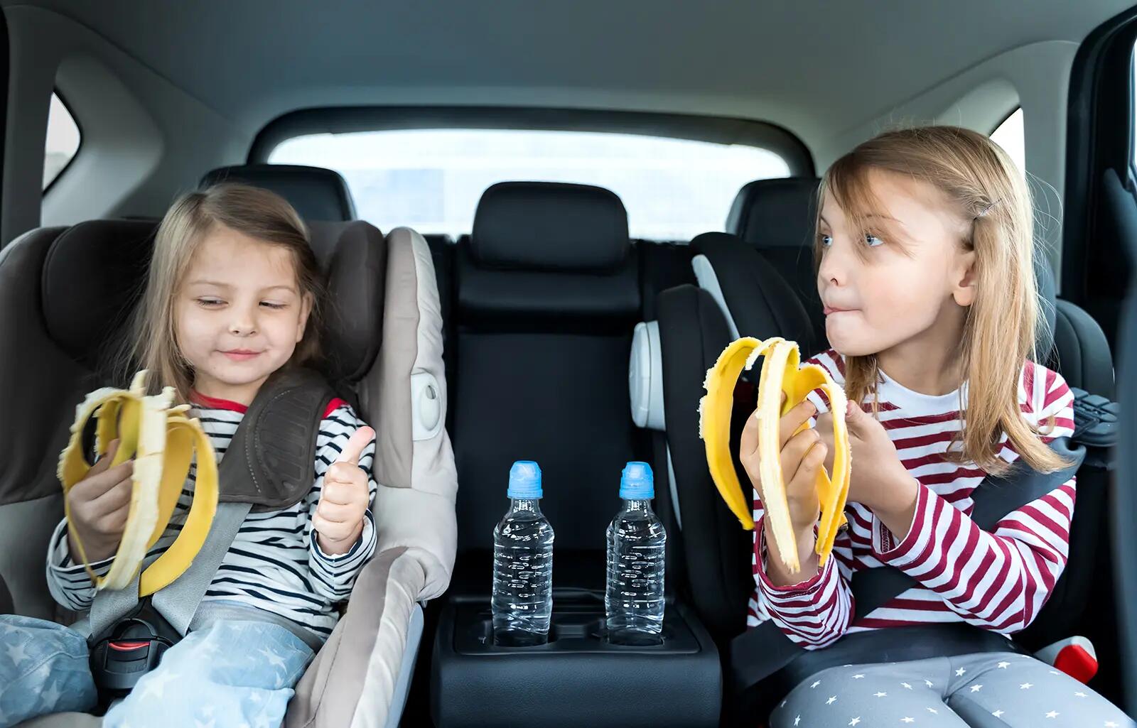Dwie dziewczynki siedzące w fotelikach jedzące banana w samochodzie
