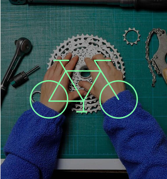 Draufsicht auf die Hände einer Person in blauem Pullover, die an einem Fahrradkassette auf einer grünen Schneidematte arbeitet. Darüber liegt die grüne Kontur eines Fahrrads als Logo.