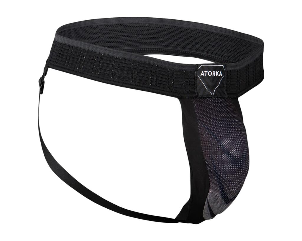 Schwarzer Tiefschutz (Jockstrap) der Marke Atorka von Decathlon auf weißem Hintergrund. Das Produkt besteht aus einem breiten, elastischen Hüftband, dünnen Beinbändern und einer vorne angebrachten, geformten Schutzkappe mit dunklem Muster. Vorne am Bund befindet sich ein rautenförmiges Aufnäher-Logo mit der Aufschrift ‚ATORKA‘.