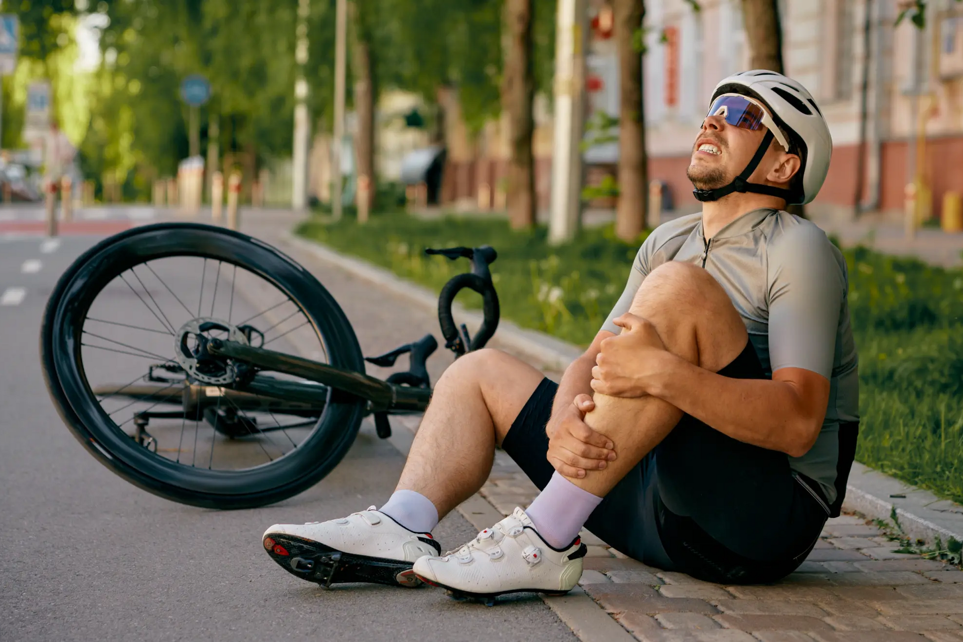 Mężczyzna trzymający się za nogę siedzący na ścieżce rowerowej rower obok