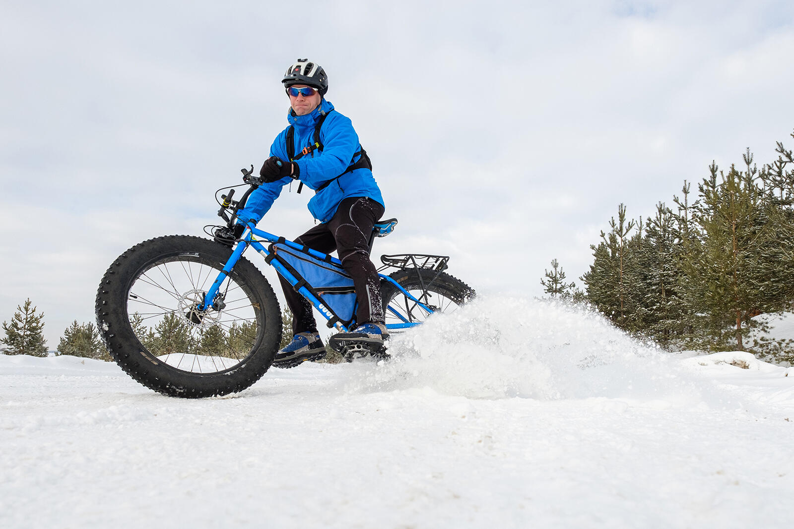 Mężczyzna w odzieży zimowej w kasku i w okularach jeżdżąct fatbikem po śniegu