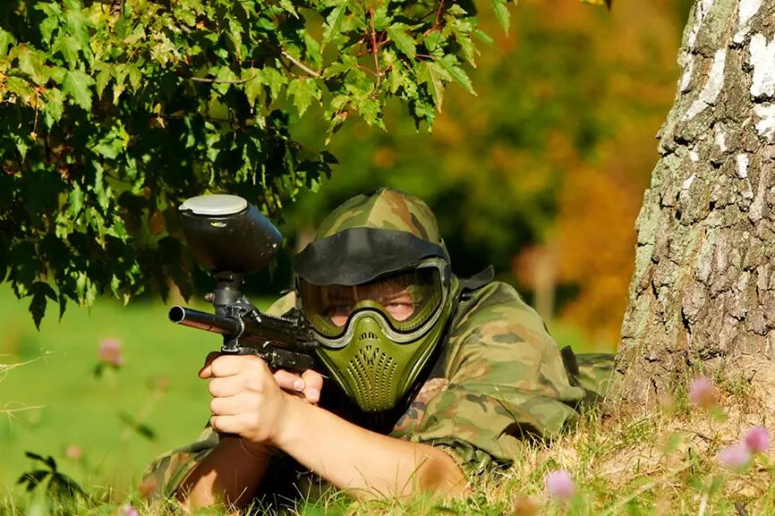 Mężczyzna leżący na trawie w kasku grający w paintball