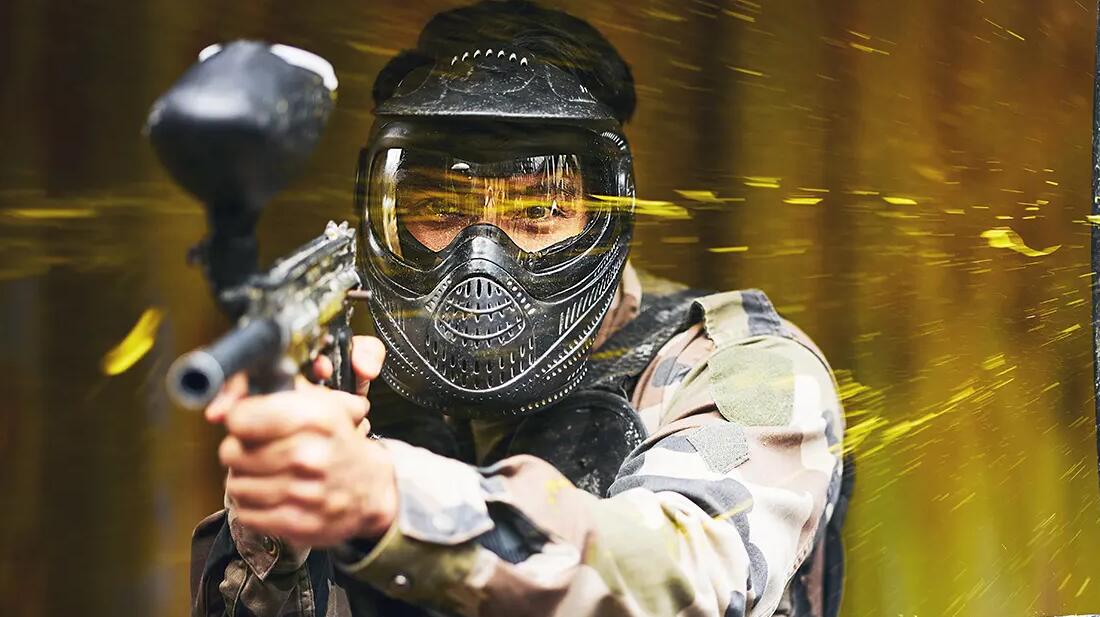 Mężczyzna w odzieży i masce do paintballa trzymający pistolet do paintballa