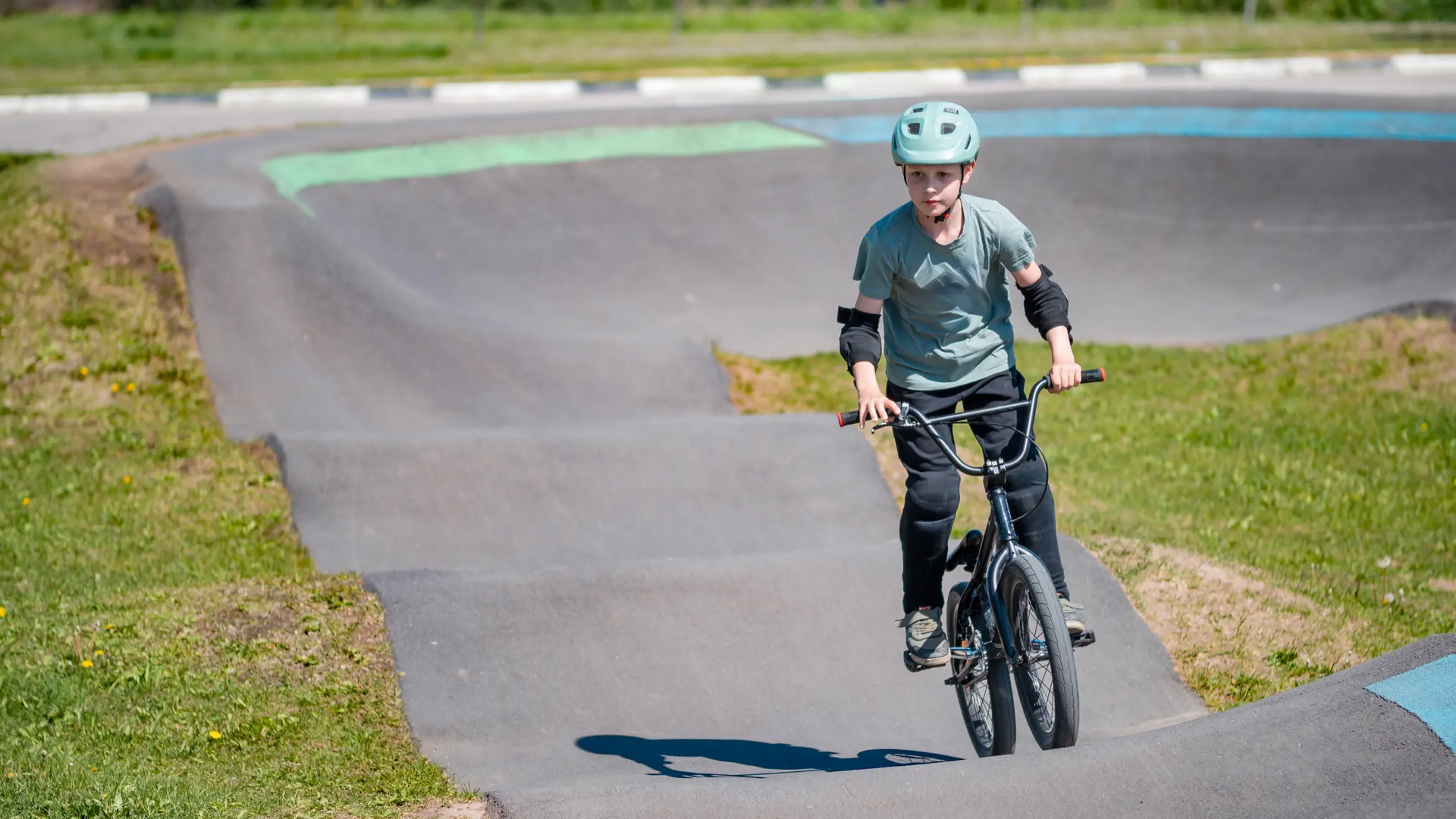 Chłopiec w ochraniaczach i w kasku jeżdżący rowerem po pumptracku