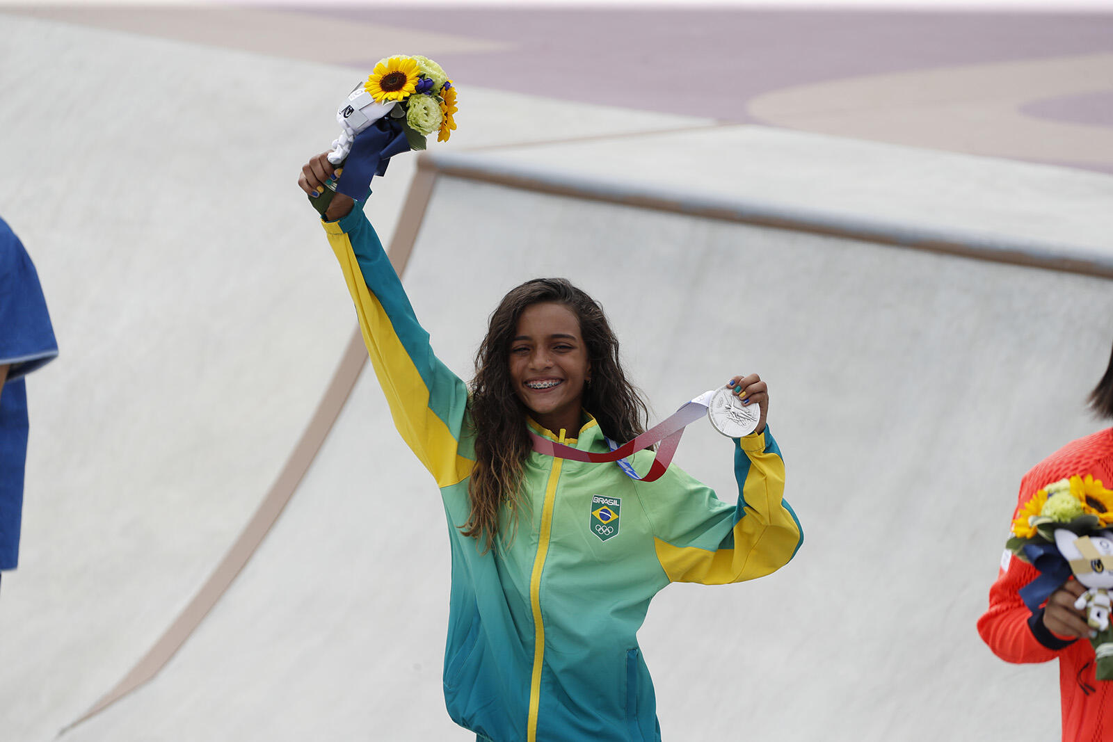 Kobieta trzymająca w jednej ręce kwiaty a w drugiej srebrny medal olimpijski