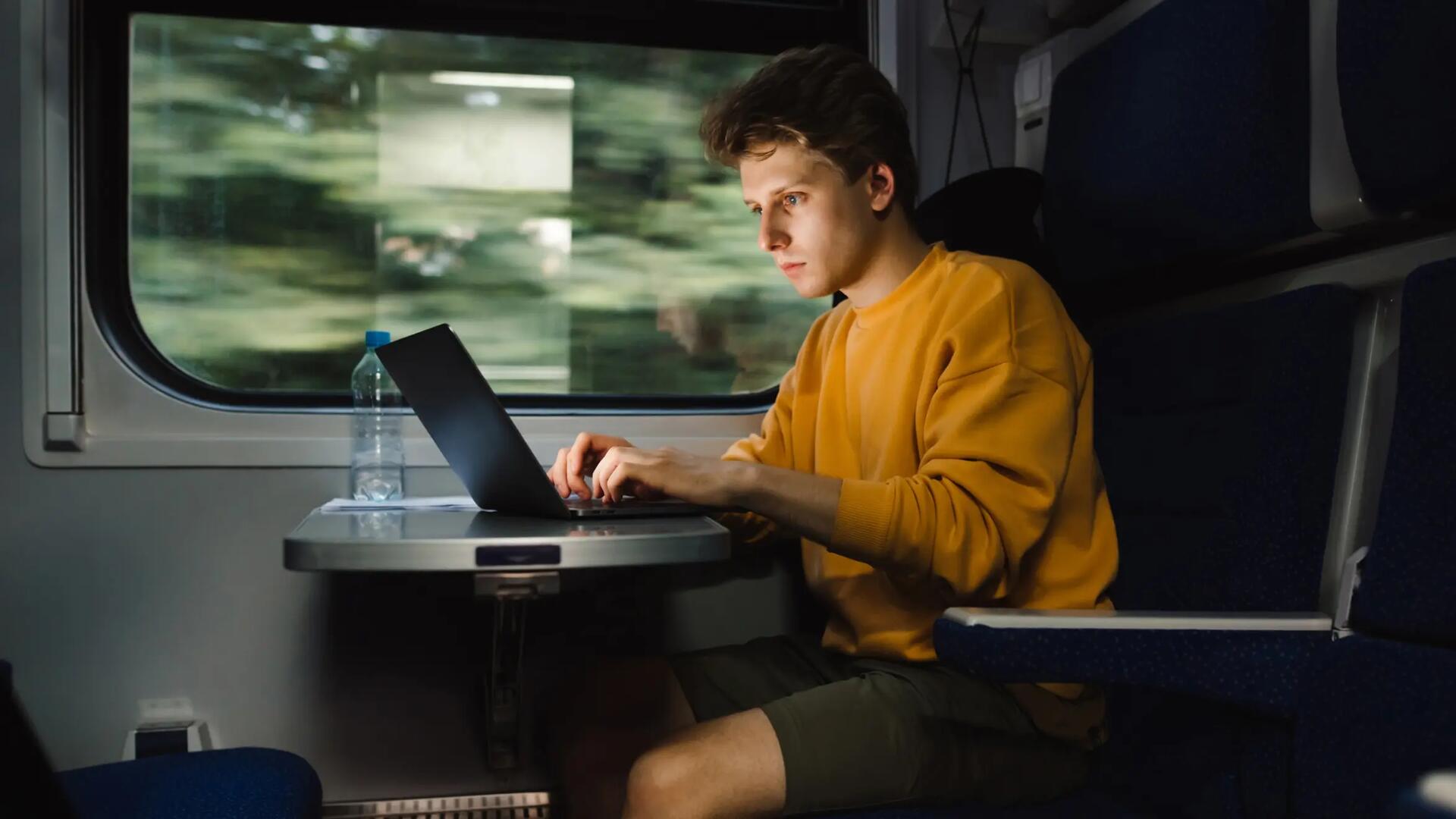 Mężczyzna pracujący na laptopie jadąc pociągiem po zmroku
