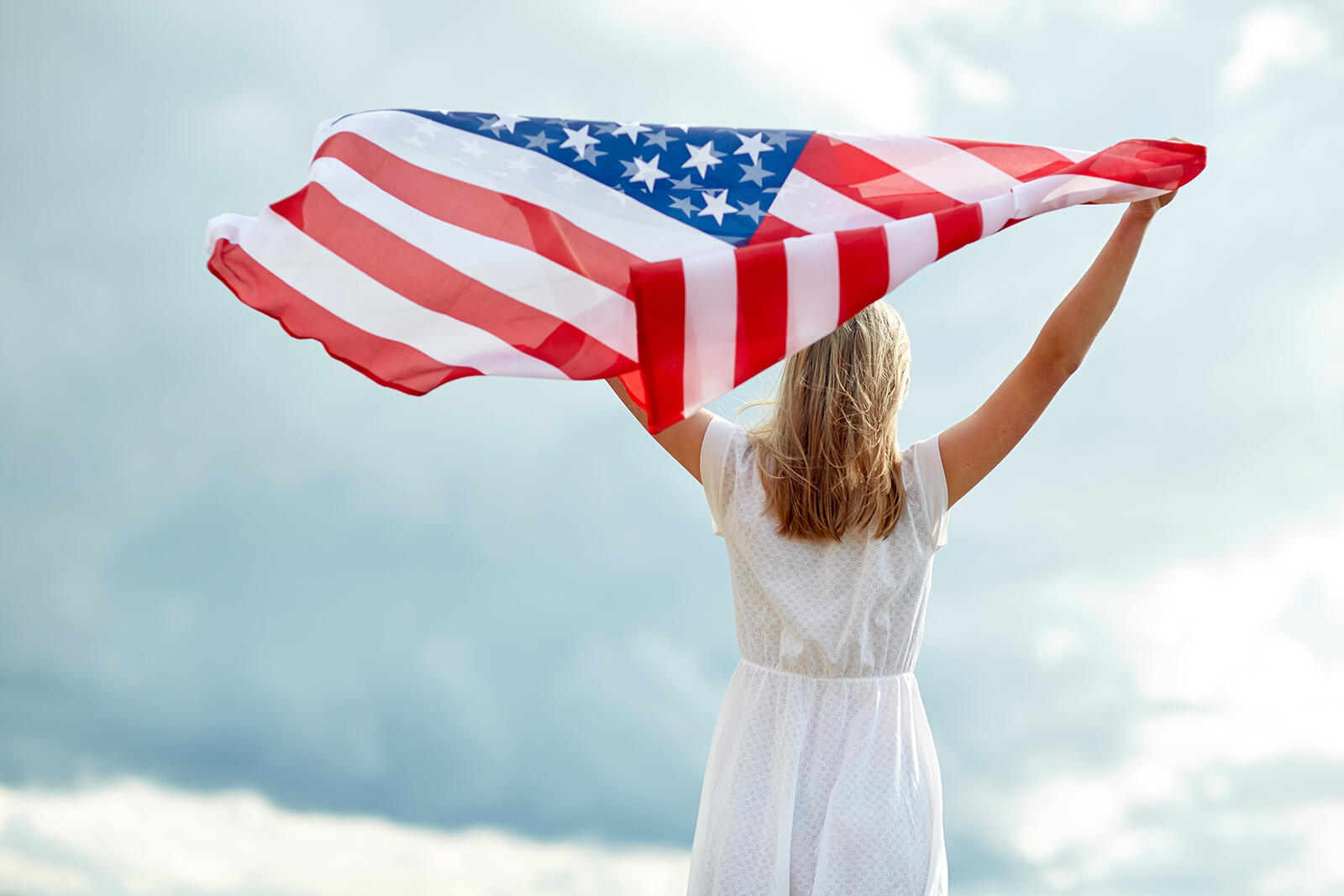 Kobieta stojąca tyłem machająca flagą USA trzymaną w rękach