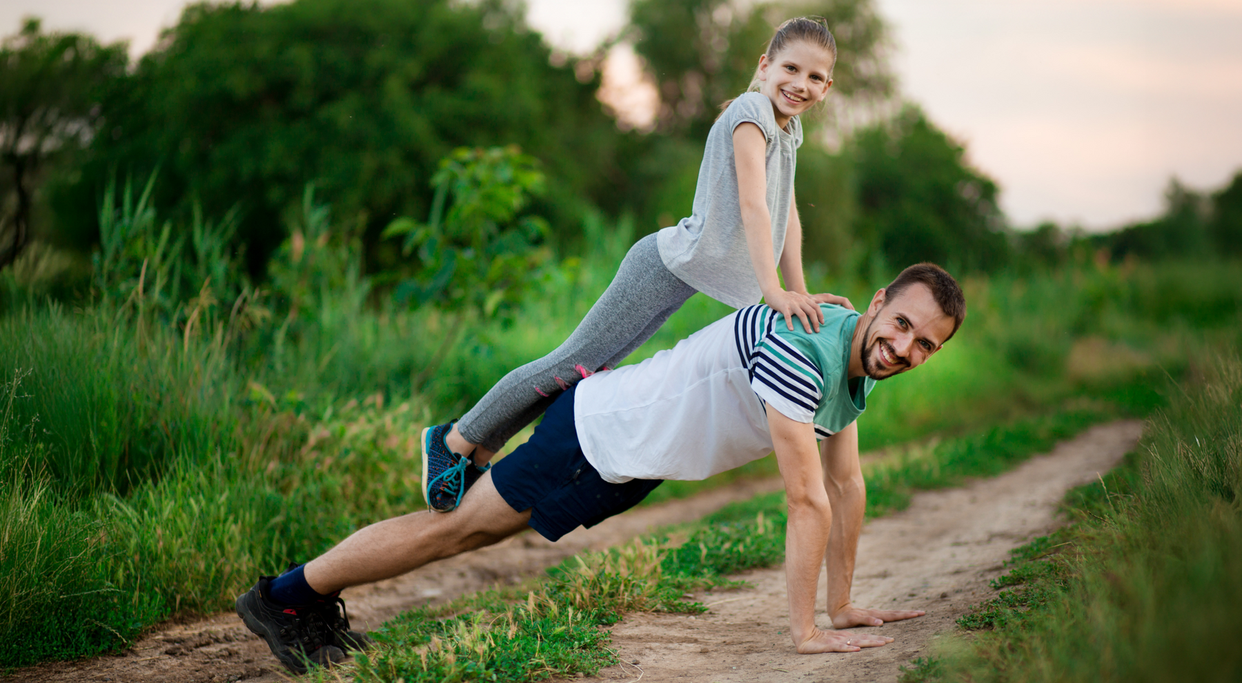 Mężczyzna z dziewczynką na plecach w pozycji plank na ziemii