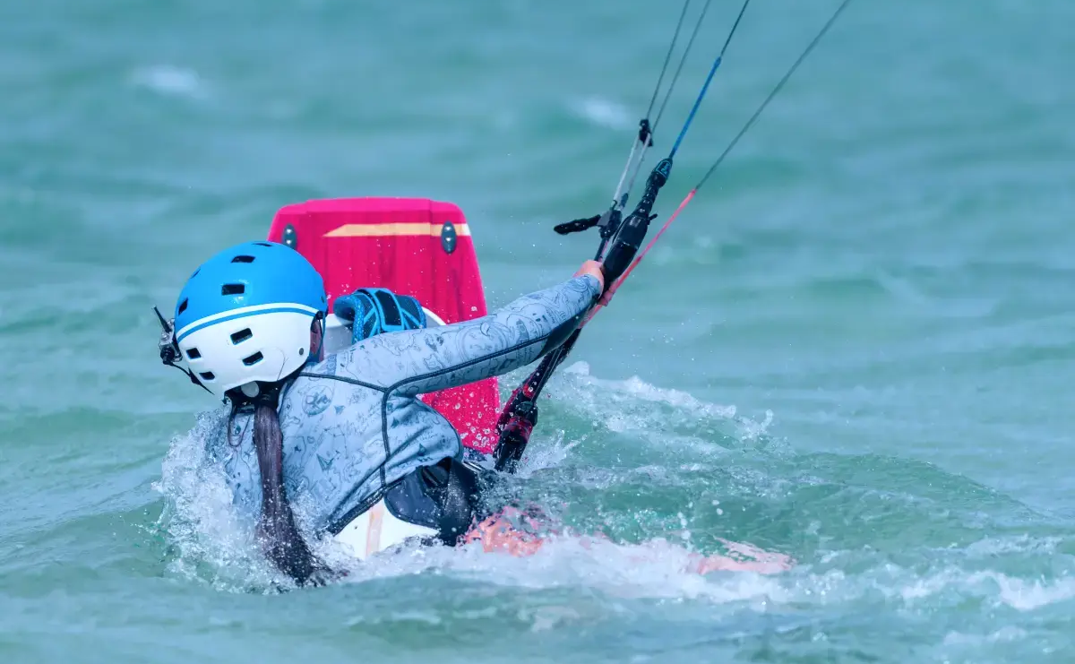 Kobieta w stroju i kasku do kitesurfingu wykonujaca body dragi podczas treningu na kitesurfingu