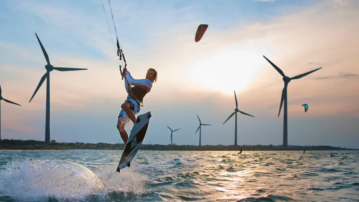 Mężczyzna trzymający bar kitesurfingowy wykonujący trik na desce kitesurfingowej
