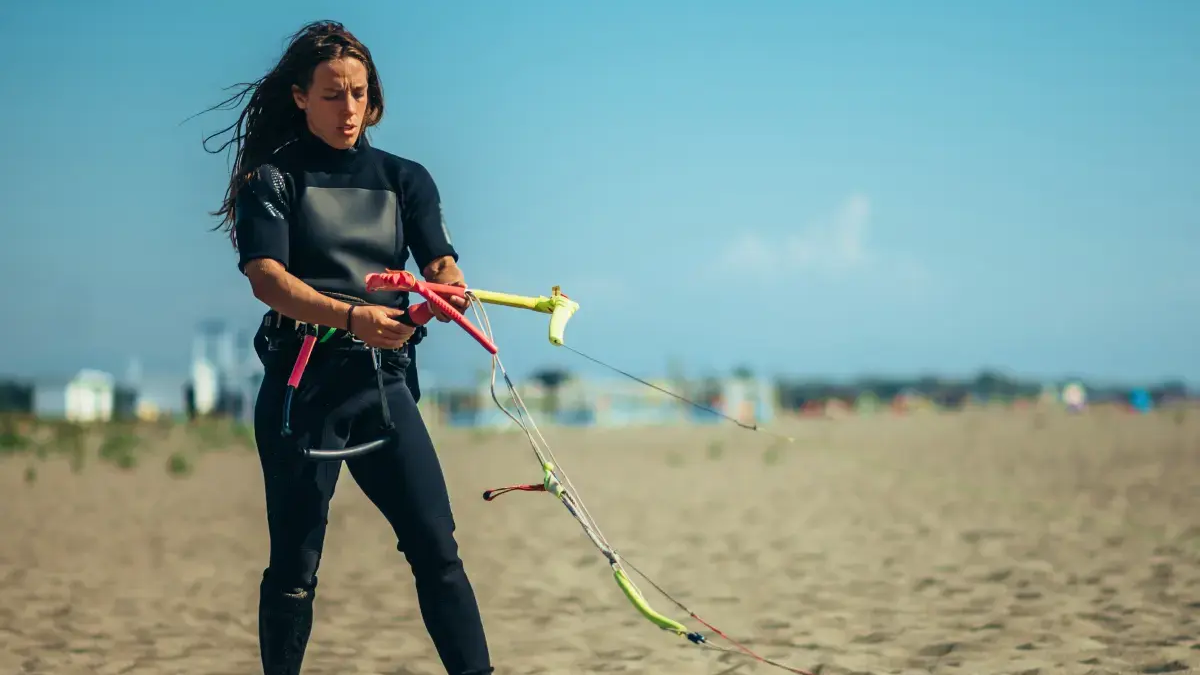 Kobieta w stroju do kitesurfingu trzymająca bar do kitesurfingu stojąc na plaży