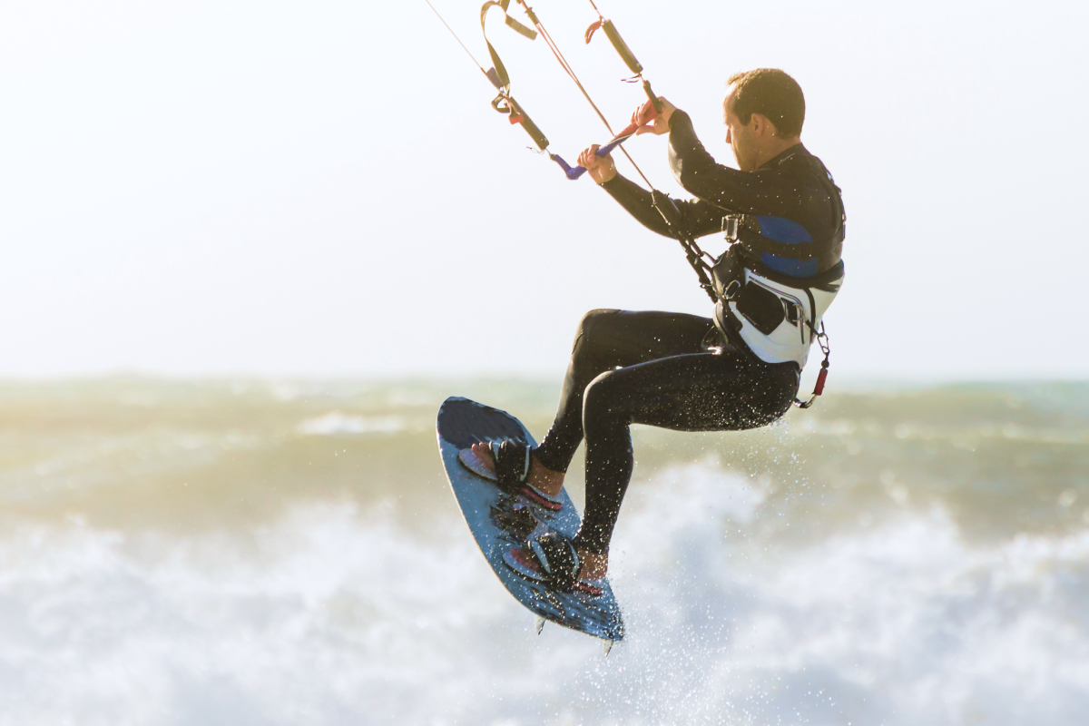 Mężczyzna w stroju kitesurfingowym trzymający bar próbując wykonać kiteloop