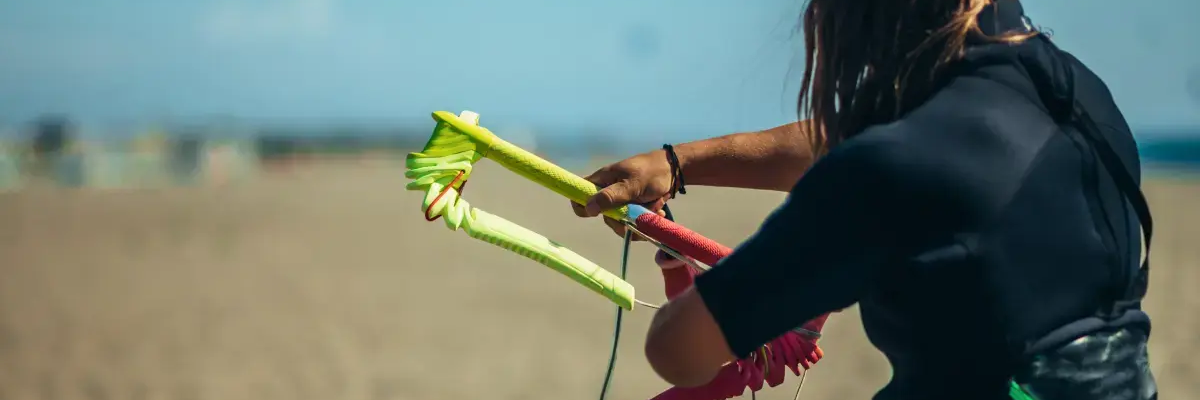 Kobieta w piance do kitesurfingu wykonująca trymowanie baru stojąc na plaży
