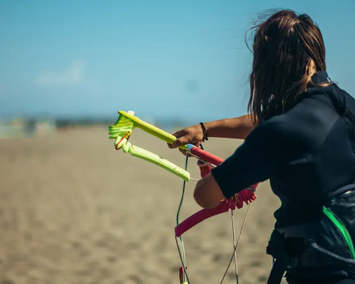 Kobieta w piance do kitesurfingu wykonująca trymowanie baru stojąc na plaży