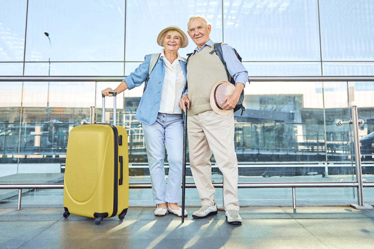 Para seniorów z walizką stojący na lotnisku
