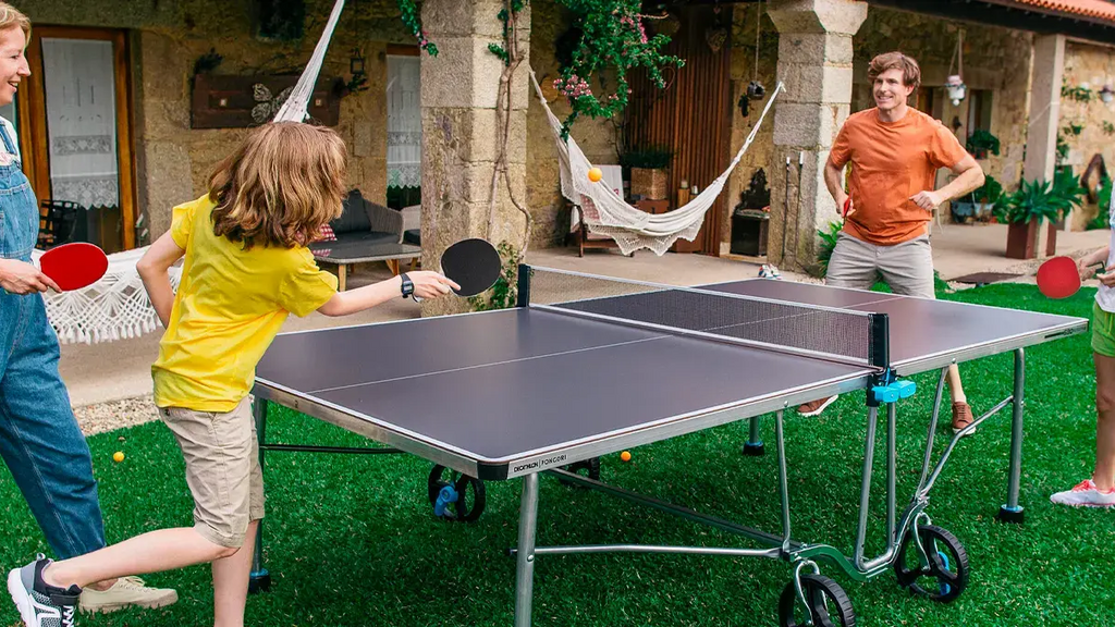 Eine vierköpfige Familie die im Garten Tischtennis an einer Platte spielen.