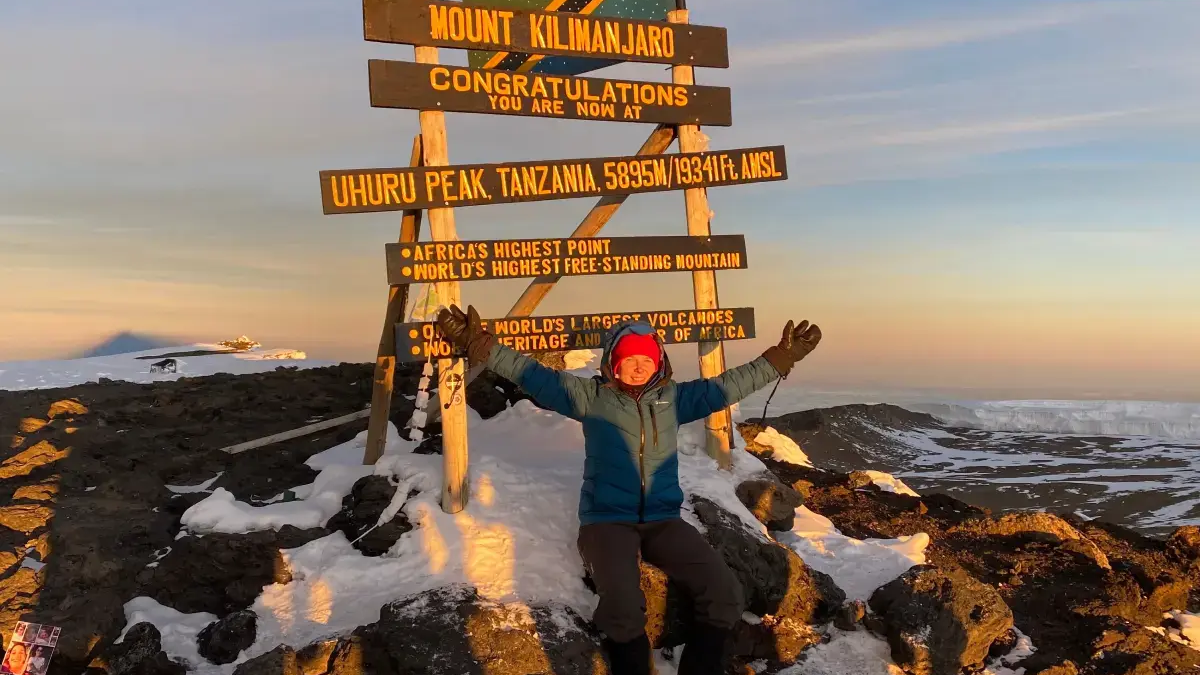 Osoba w odzieży trekkingowej siedząca na szczycie Kilimandżaro