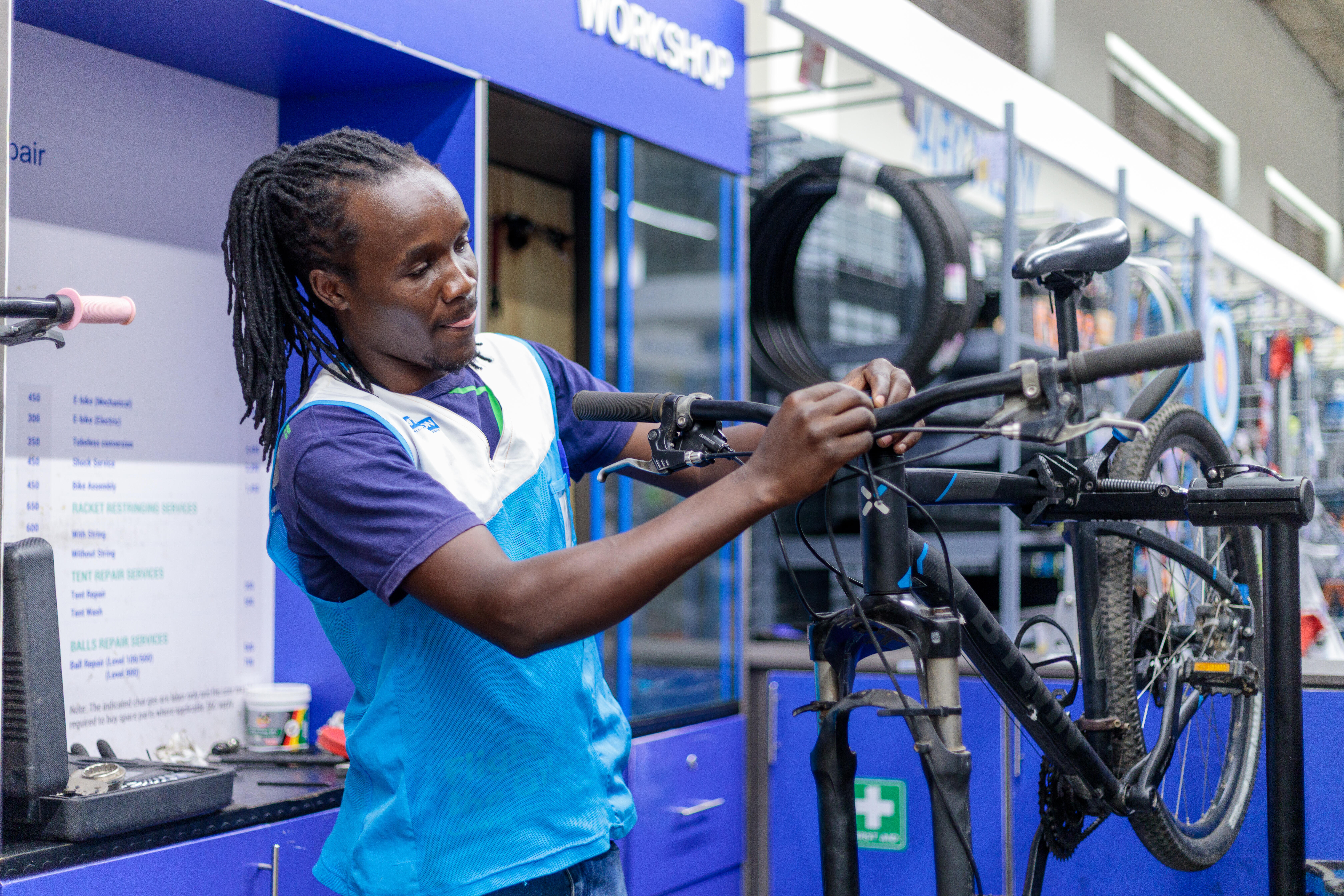 A worker at a Decathlon store carefully inspects a bicycle as he prepares it for service or repair, using specialized tools.