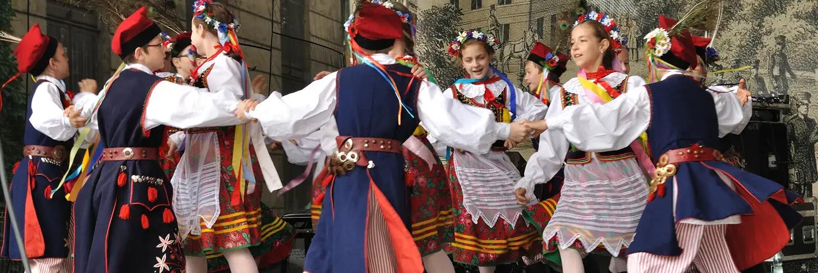 Mężczyźni i kobiety w strojach ludowych tańczący krakowiaka