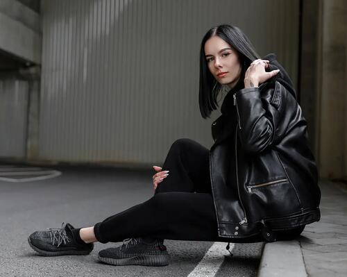 Kobieta w ramonesce i w dresach siedząca na krawężniku