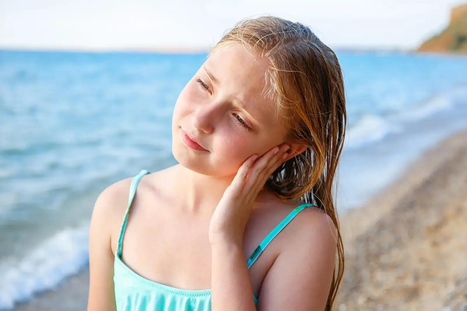 Dziewczynka w stroju kąpielowym na plaży trzymająca się za ucho