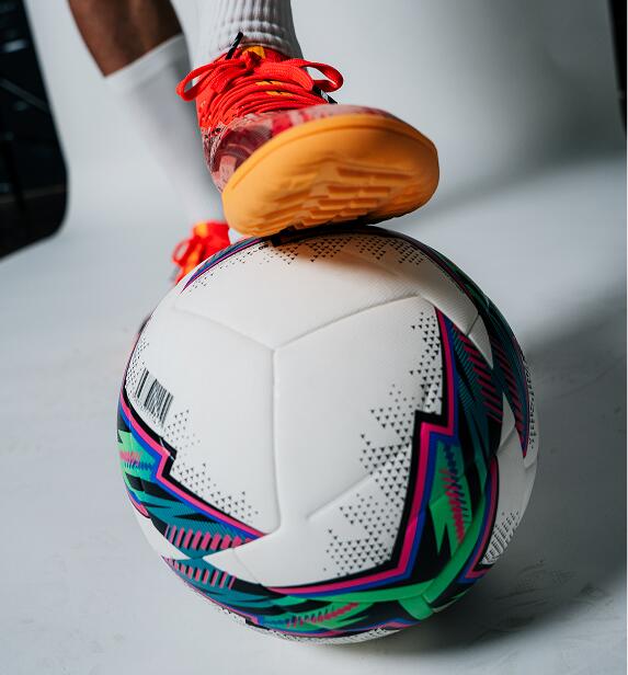 Nahaufnahme eines Fußes in einem roten Kipsta CLR Hallenschuh, der auf einem gemusterten Kipsta Fußball steht.