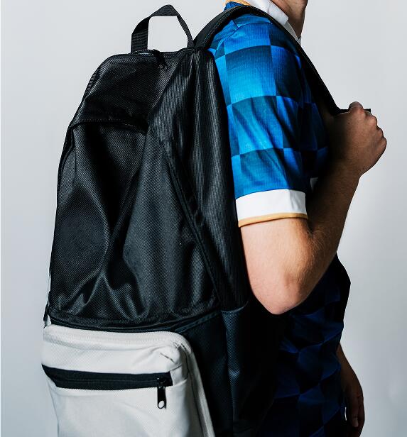 Seitenansicht eines Mannes mit einem schwarz-weißen Sportrucksack und Two Stripes United Heimtrikot vor hellem Hintergrund.