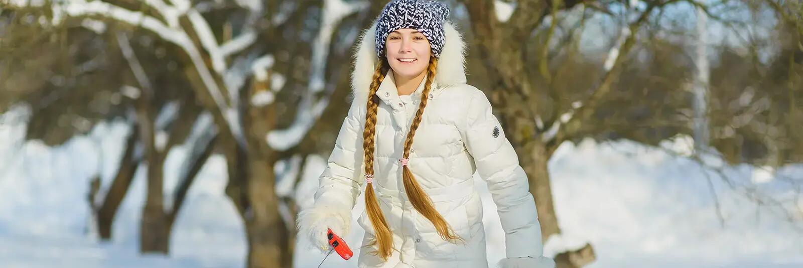 Dziewczynka w kurtce zimowej idąca z psem na smyczy po śniegu