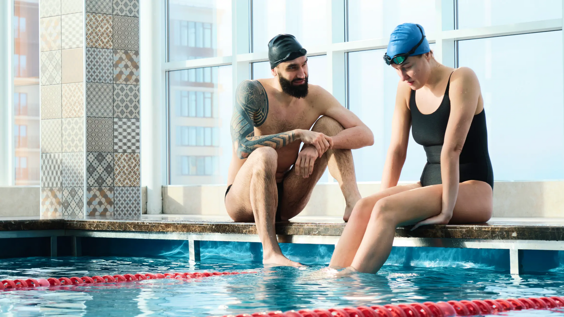 Mężczyzna i kobieta w czepkach siedzący nad basenem moczący nogi