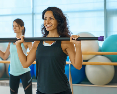 Kobiety ćwiczące z drążkiem do pilatesu na sali