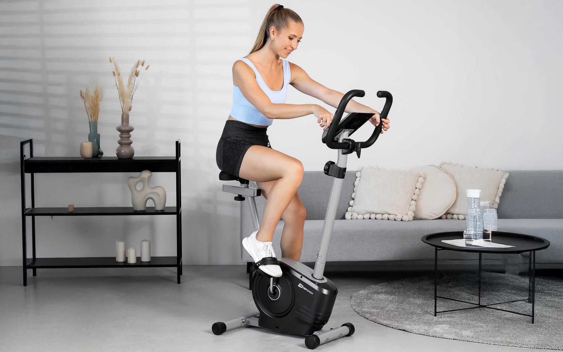 Kobieta w odzieży sportowej jeżdżąca na rowerze stacjonarnym w domu