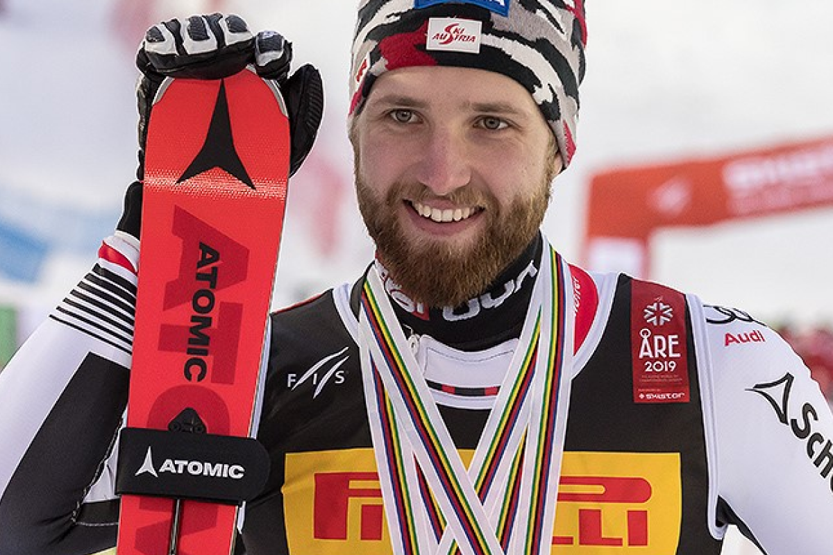 Mężczyzna z medalami na podium w ręku narty