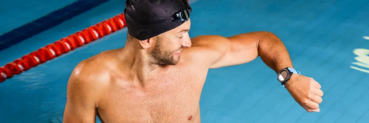 Mężczyzna w czepku patrzący na smartwatch do pływania stojący w basenie