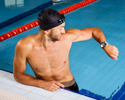 Mężczyzna w czepku patrzący na smartwatch do pływania stojący w basenie