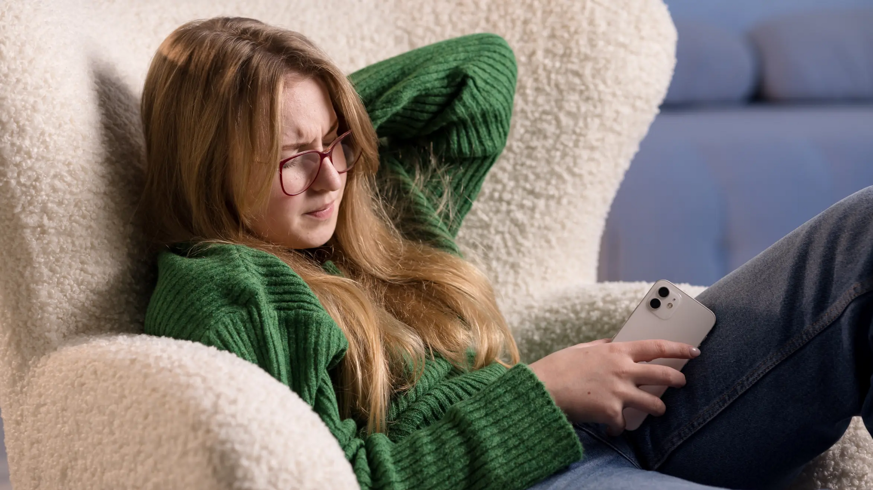 Dziewczyna siedząca na fotelu dotykająca się za kark w drugiej ręce telefon