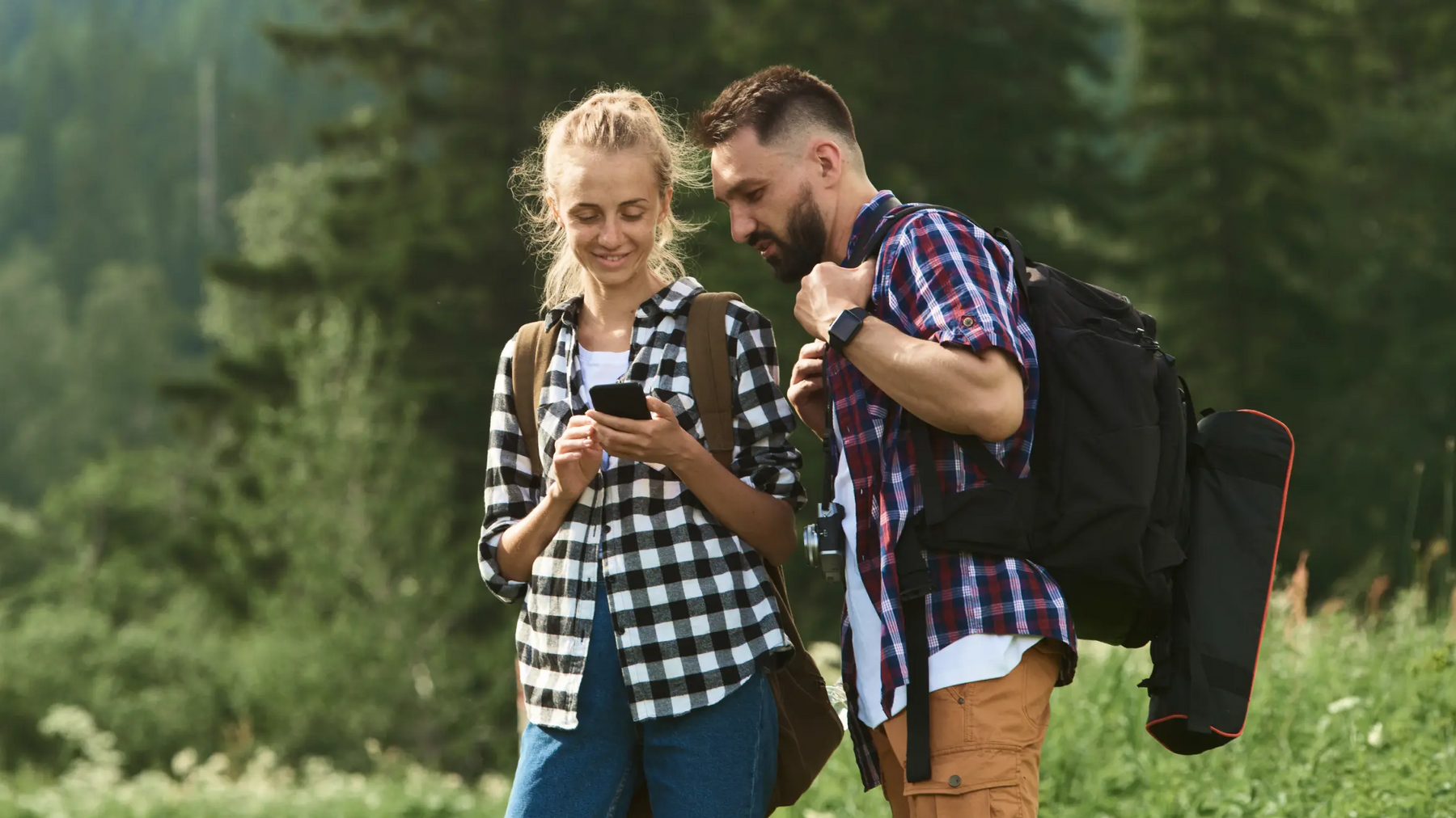 Para z plecakami w lesie patrząca na nawigację w telefonie