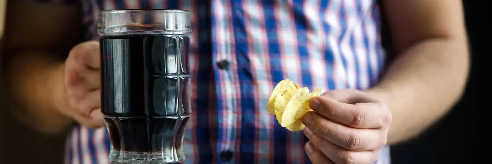 Mężczyzna trzymający w jednej ręce kufel z napojem w drugiej chipsy
