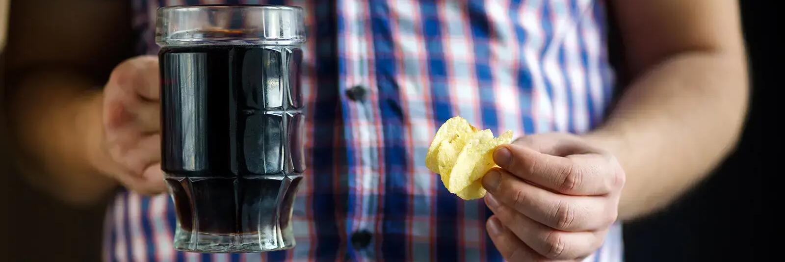 Mężczyzna trzymający w jednej ręce kufel z napojem w drugiej chipsy