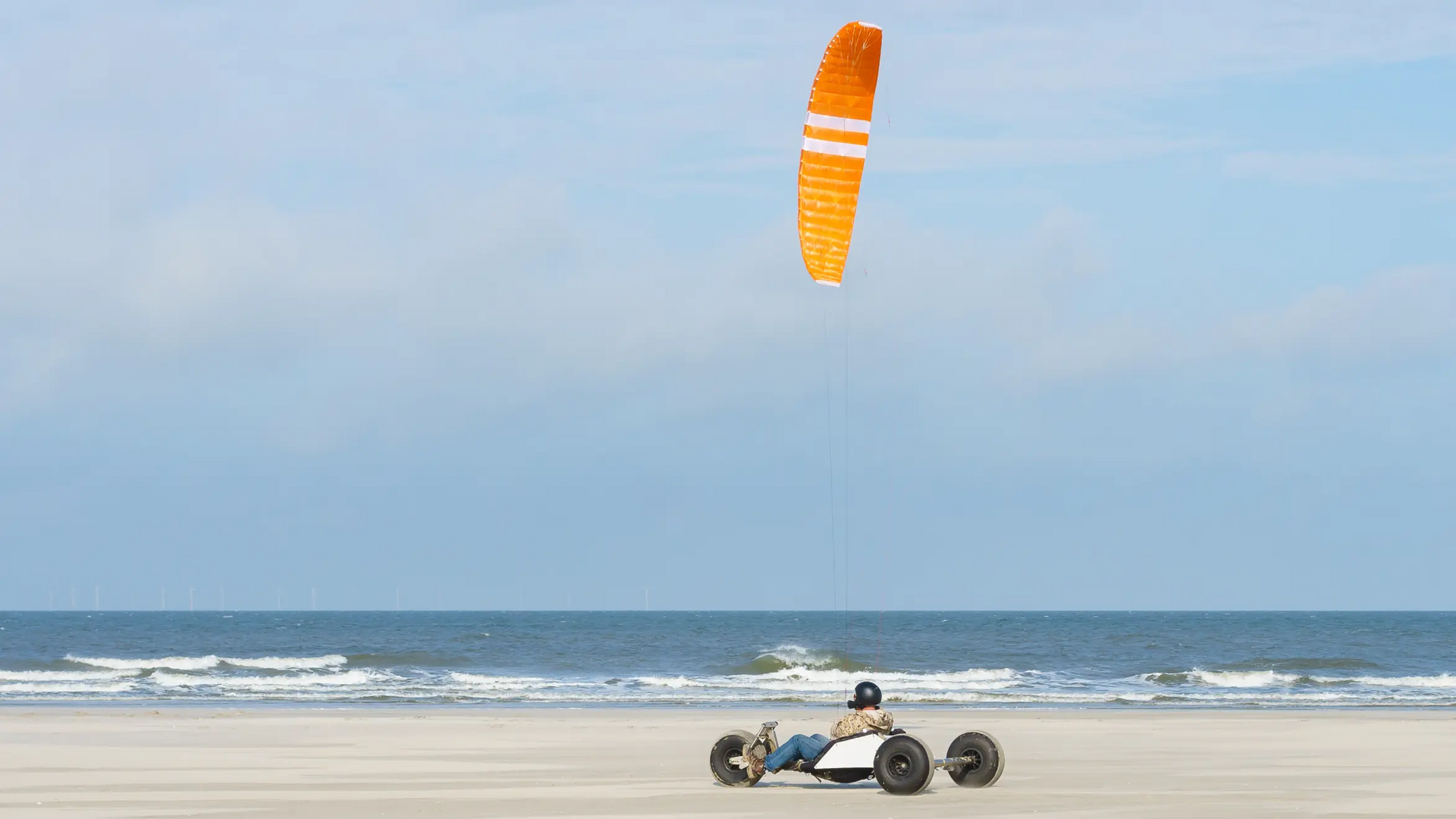 Osoba w wózku na trzech kołach z latawcem trenująca na plaży kitebuggy