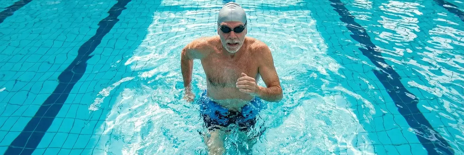 Mężczyzna trenujący aqua jogging w basenie z obciążeniem w czepku i w okularach do pływania