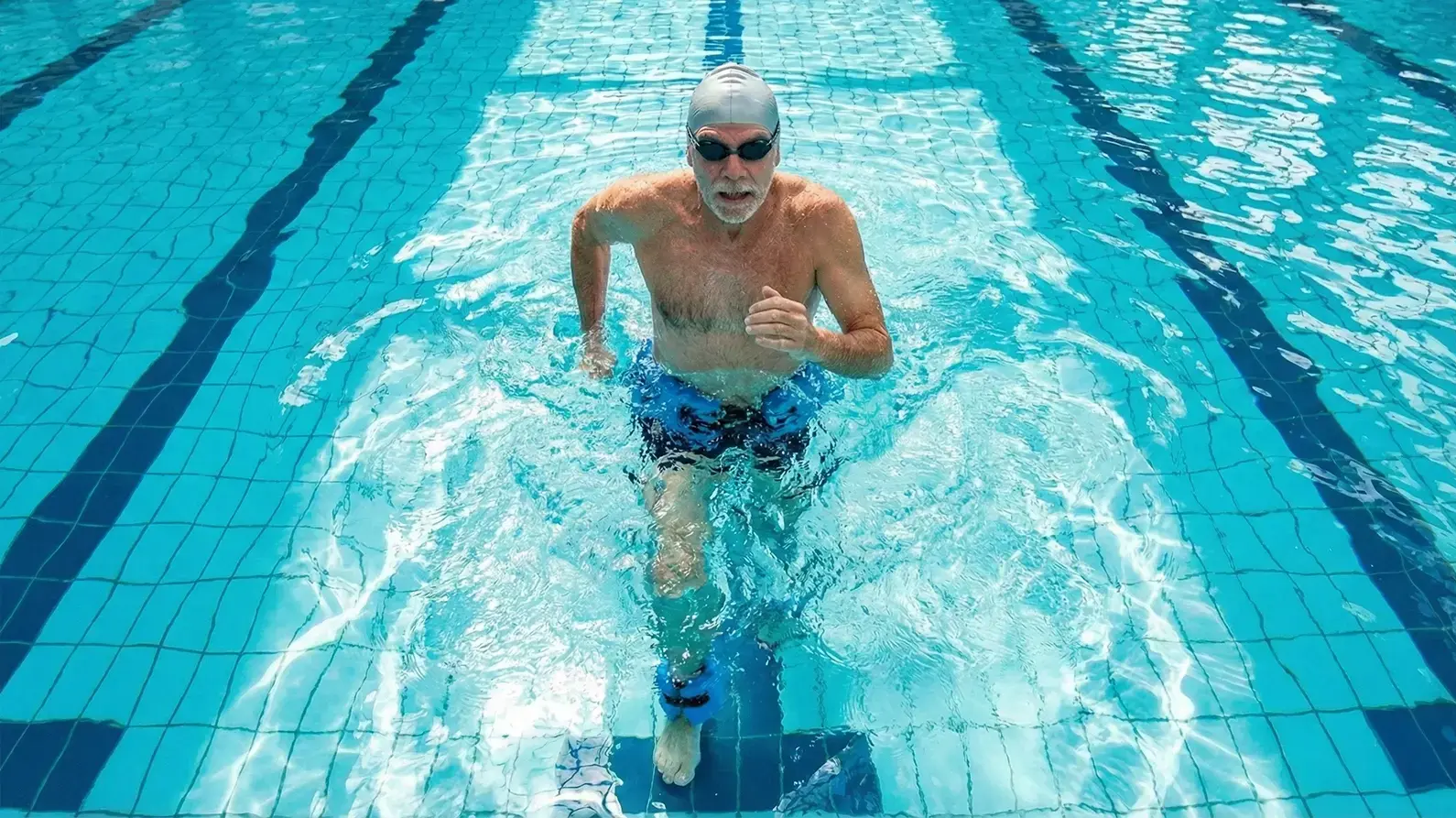 Mężczyzna trenujący aqua jogging w basenie z obciążeniem w czepku i w okularach do pływania