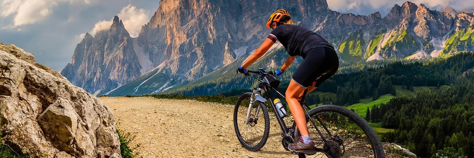Kobieta w kasku na rowerze mtb z błotnikiem z przodu jadąca po terenie górzystym