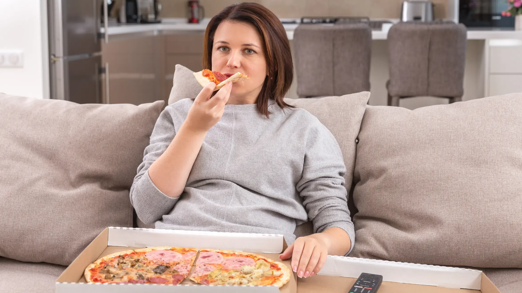 Kobieta siedząca na kanapie jedząca pizzę