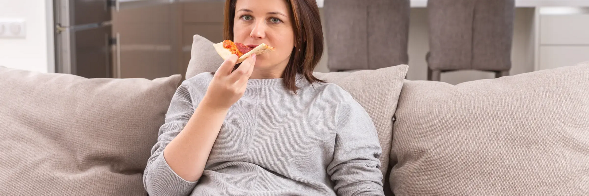 Kobieta siedząca na kanapie jedząca pizzę