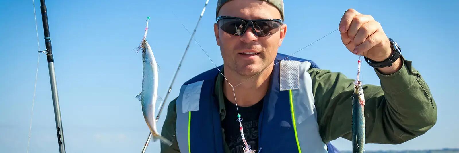 Mężczyzna na łódce trzymający w ręku wędkę ze złowionymi śledziami