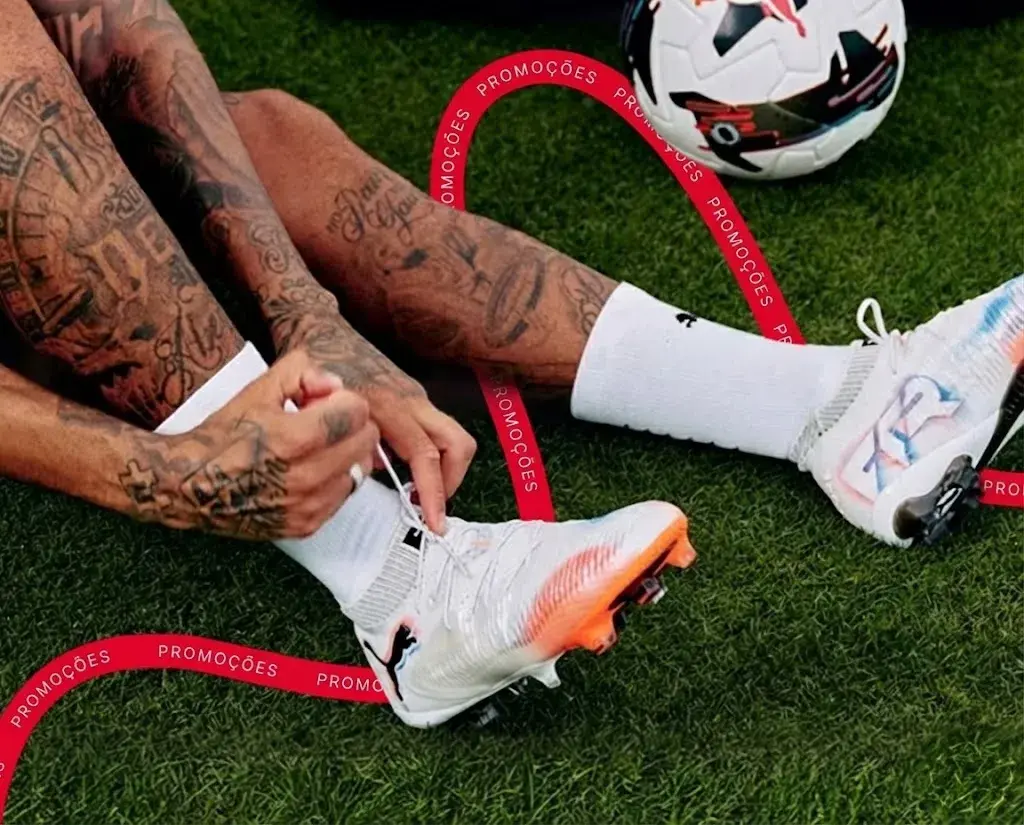 Jogador de futebol a apertar os atacadores das suas novas chuteiras brancas Puma num campo de relva natural.