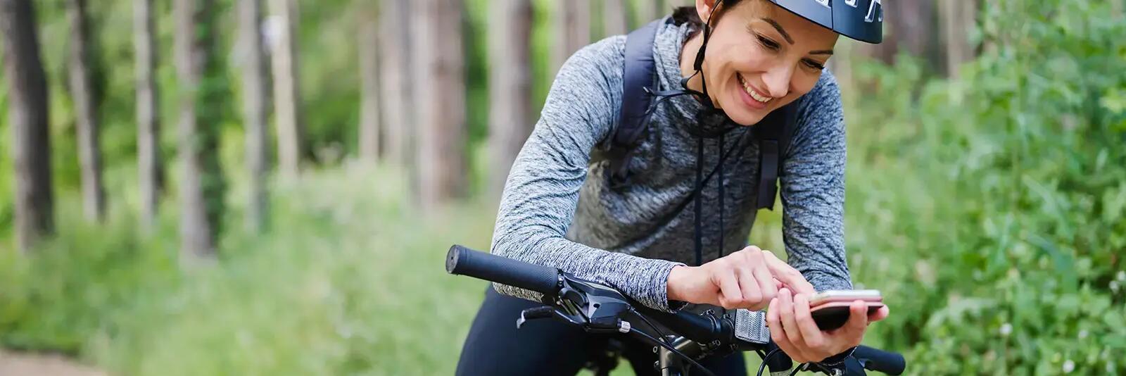 Kobieta w kasku sprawdzająca coś w telefonie na rowerze